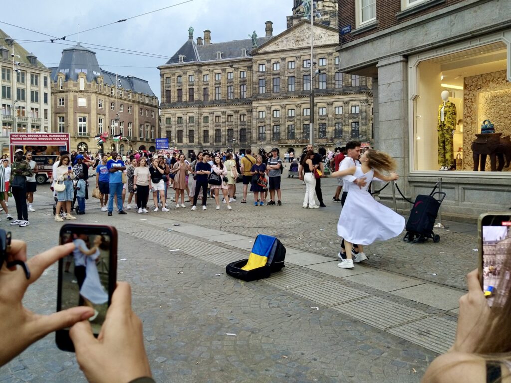 Dancing couple in front of a high-end fashion shop by the Dam in Amsterdam, people around watching and recording with their phones. Photo by Sophie Huijts