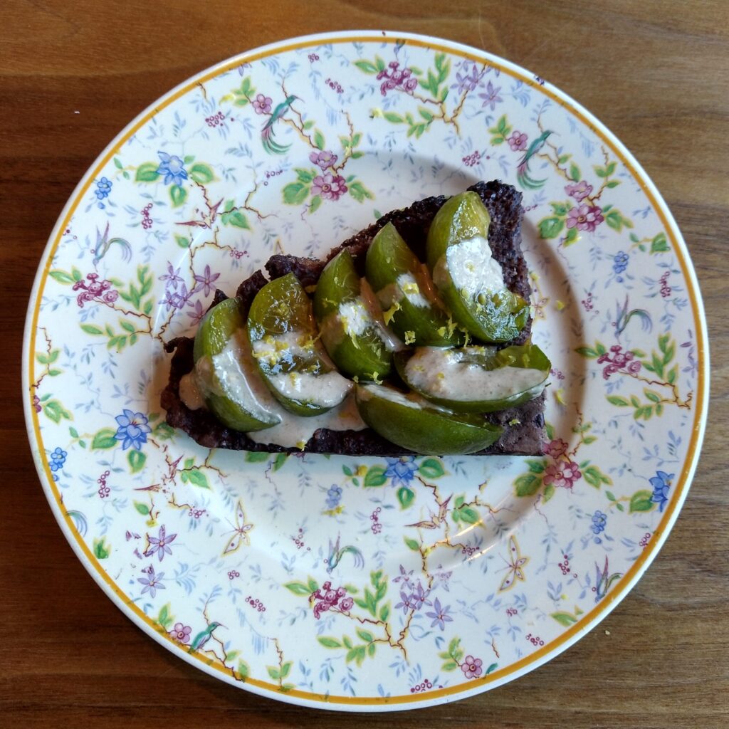 Pain perdu made with tourte de seigle (French rye bread) and a cocoa-egg-water-milk batter with green Reine Claude plum, tahini and lemon zest on top, served on an saucer with flower pattern, prepared and photo by Sophie Huijts