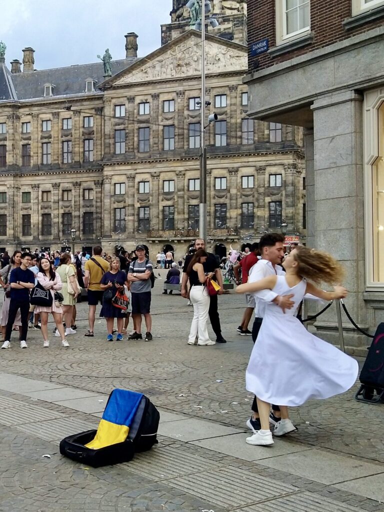 Dancing couple in front of a high-end fashion shop by the Dam in Amsterdam, people around watching and recording with their phones. Photo by Sophie Huijts